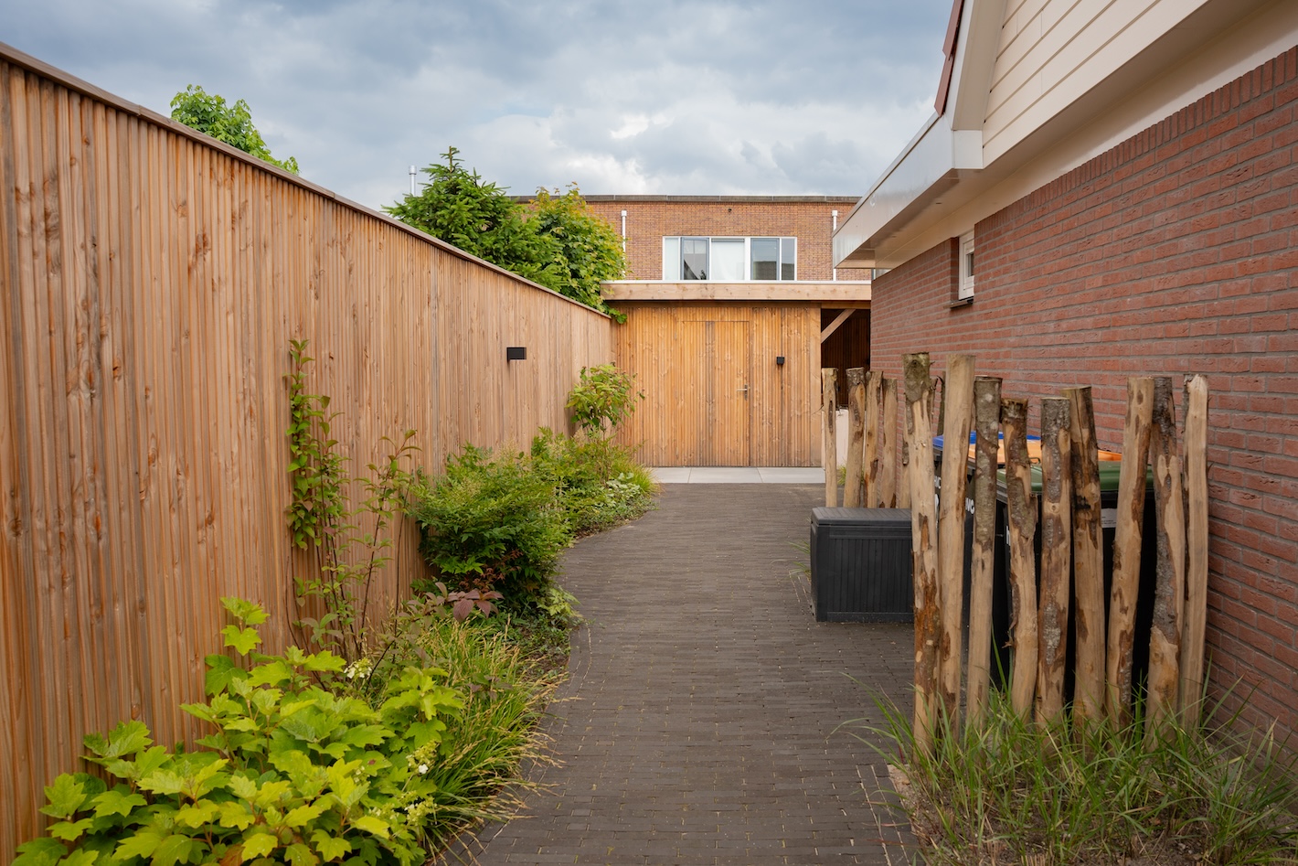 Sfeervol aangelegde tuinpad met houten schutting en beplanting, onderdeel van een tuinrenovatie door Snijers Tuinen.